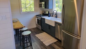 A compact kitchen with a stove, microwave, sink, and stainless steel refrigerator. There are wooden stools and a rug on the floor. - Relaxing retreat in the country (perth east)