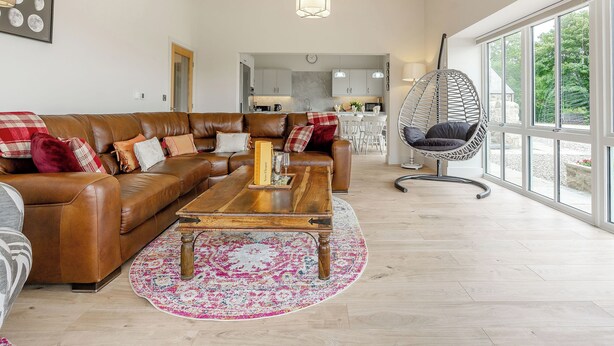 A spacious living room with a brown leather sofa, a wooden coffee table, and a large window offering a view of the outdoors. - A fabulous place to come and make memories whatever the occasion. (Stanhope)