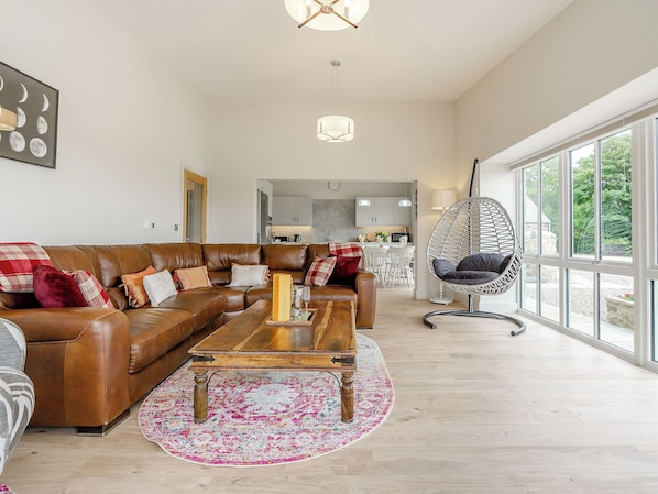 A spacious living room with a brown leather sofa, a wooden coffee table, and a large window offering a view of the outdoors.