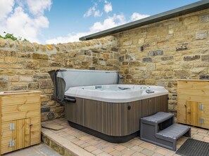 Un jacuzzi con terraza de madera, pared de piedra y un mueble de madera.