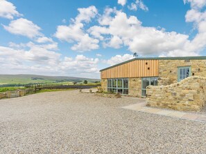 A stone building with a wooden extension, gravel driveway, and a view of rolling hills.