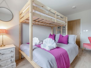 Una cama litera con estructura de madera, una mesita de noche con cajones, una lámpara y una silla.
