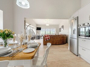 A modern kitchen with a dining area, a hanging chair, and a large window. - A fabulous place to come and make memories whatever the occasion. (Stanhope)