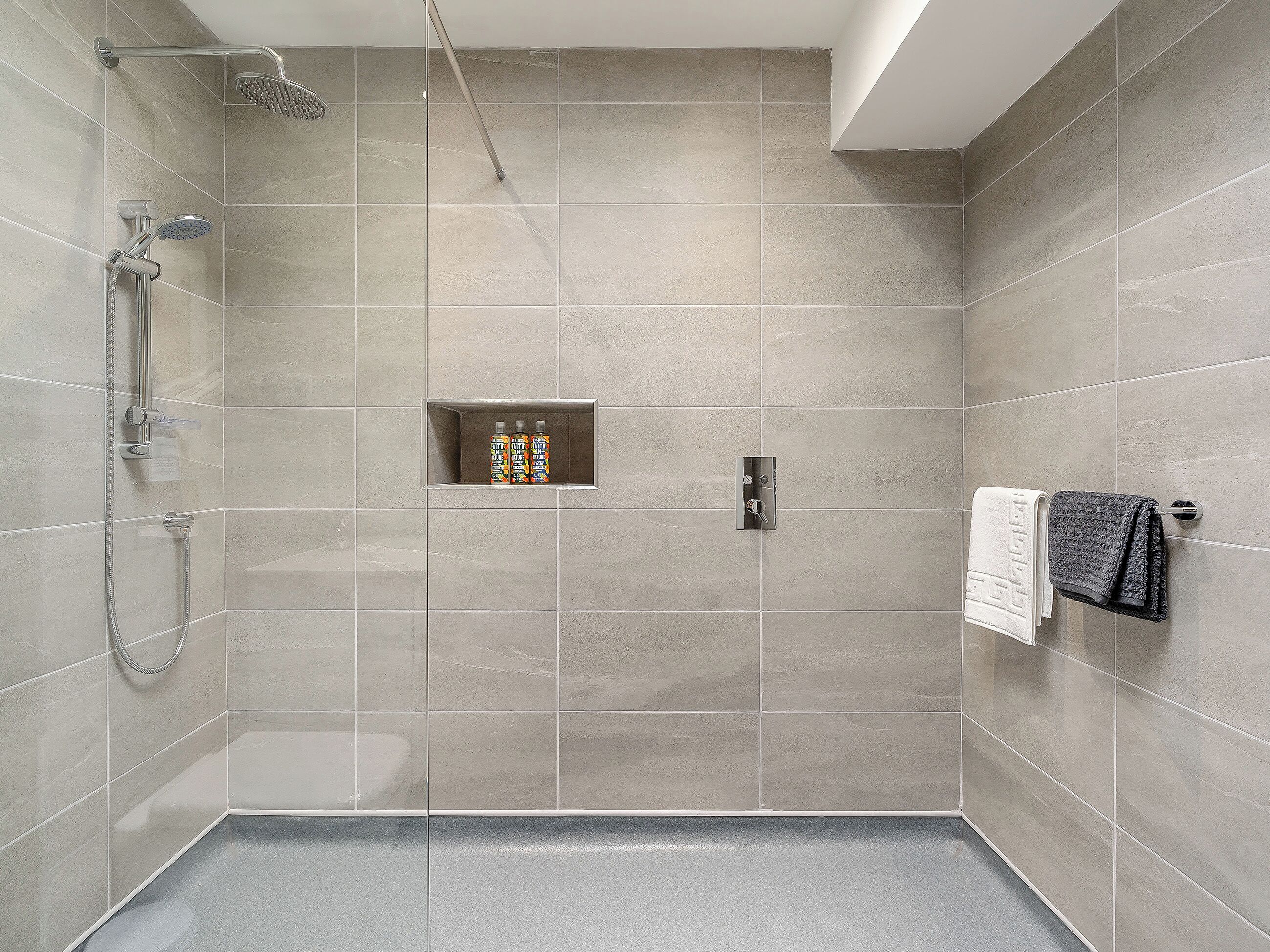 A modern shower with a handheld showerhead and a wall-mounted faucet.
