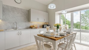 A modern kitchen with white cabinets, a marble backsplash, and a dining area with white chairs and a wooden table. - A fabulous place to come and make memories whatever the occasion. (Stanhope)