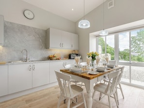 A modern kitchen with white cabinets, a marble backsplash, and a dining area with white chairs and a wooden table.