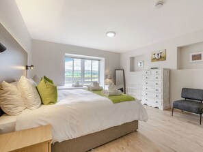A bedroom with a large bed, a dresser, a chair, and a window with a view.
