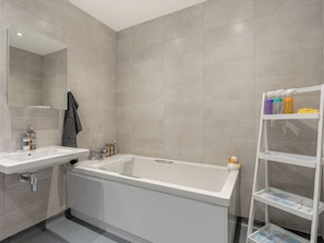 A bathroom with a bathtub, a sink, a mirror, and a shelf with toiletries.