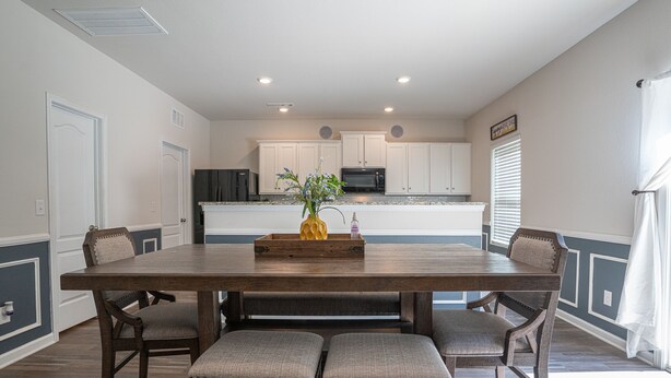 A dining area with a wooden table and four upholstered chairs, a vase with flowers, and a tray with a bottle and a candle. - Stunning 5 BD Home away from Home! 15 min to uptown (Charlotte)