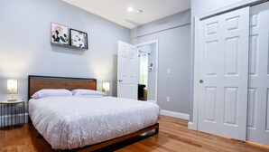 Un dormitorio con cama, lámparas de noche, una puerta y un cuadro colgado en la pared.