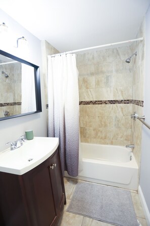 Ein Badezimmer mit weißem Waschbecken, dunklen Holzschränken, einer Dusche mit beige gefliesten Wänden und einer weißen Badewanne.