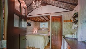 Une chambre avec un plafond en bois, un lit recouvert d’une couverture verte, une table de chevet, une fenêtre donnant sur un beau paysage et une porte en bois.