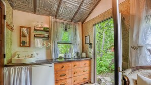 Une cuisine compacte comprenant un évier, un petit réfrigérateur et un meuble en bois doté de tiroirs. Une fenêtre offre une vue sur la verdure environnante.