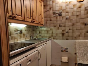 A kitchen with wooden cabinets, a granite countertop, a dishwasher, and a tiled backsplash with decorative tiles.