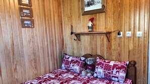Ein Zimmer mit Holzwänden, einem Bett, einer Ablage mit Bilderrahmen und einer kleinen Figur.