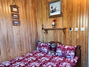 A wooden-paneled room with a bed, a shelf with a picture frame, and a small figurine.