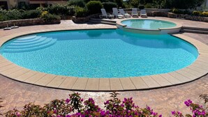A swimming pool with a curved edge, surrounded by a stone deck and a flower bed with purple flowers. - Stunning Apartment With Pool in Olbia, Sardinia (Olbia)