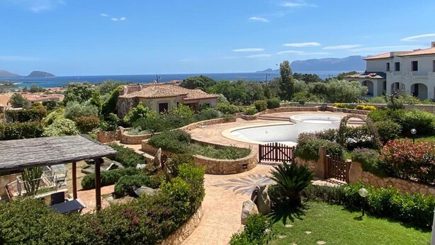 A landscaped garden with a pool, surrounded by buildings with Mediterranean architecture, overlooking a coastal area. - Stunning Apartment With Pool in Olbia, Sardinia (Olbia)