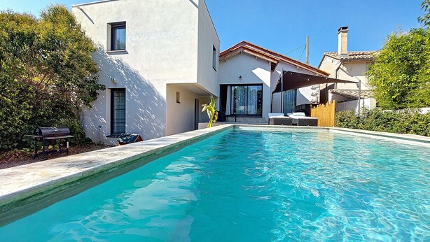 Una casa moderna con piscina, un patio con mobiliario exterior y un gran ventanal con vistas a la piscina.