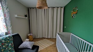 Una sala de estar acogedora con un sofá negro, una cuna para bebé, una lámpara de fibra y una pared de acento verde.