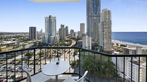 A balcony with a table and chairs, overlooking a cityscape with high-rise buildings and a beach. - Ocean View 2-Bed Studio In the Heart of Surfers (Surfers Paradise)