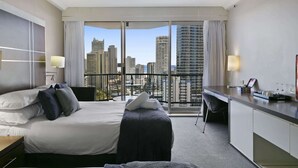 A hotel room with a bed, a desk, and a view of city buildings. - Ocean View 2-Bed Studio In the Heart of Surfers (Surfers Paradise)