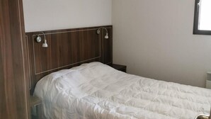 A single bed with a wooden headboard and two bedside lamps, a wooden wardrobe, and a window with blinds. - Floor -2, view valley, swimming pool, hammam, terrace, parking, tv, 50m², Pra Loup (Jausiers)
