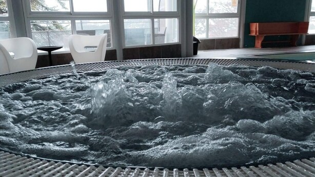 Ein Whirlpool mit gefliestem Boden und Blick ins Freie durch große Fenster.