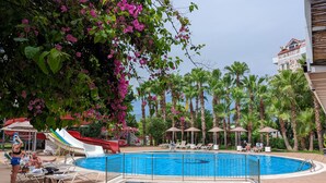 A swimming pool with lounge chairs, a slide, and palm trees. - UK Hotels Kiriş (Kemer)