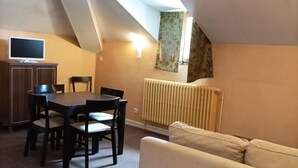 Een loft-achtige kamer met een eethoek, een bank, een radiator en een televisie op een kast.