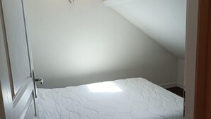 Een kleine kamer met een enkel bed, schuine wanden en een dakraam.