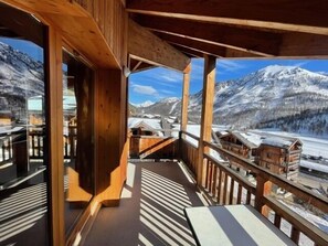 A wooden balcony with a view of snow-covered mountains and a village below.