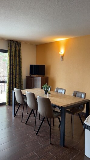 A dining area with a wooden table, six chairs, a television, a wall-mounted light, and a potted plant. - Floor -2, view valley, swimming pool, hammam, terrace, parking, tv, 50m², Pra Loup (Jausiers)