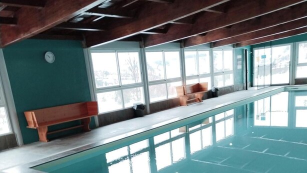 Piscina interior com água cristalina, bancos ao longo das paredes e amplas janelas que permitem a entrada de luz natural.