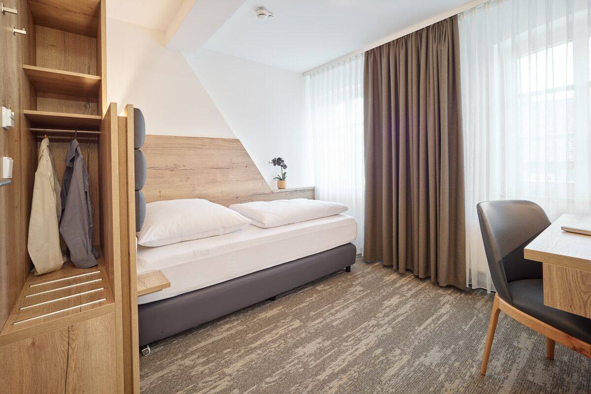 A hotel room with a bed, a desk, and a wardrobe.