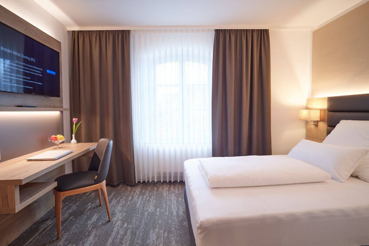 A hotel room with a bed, desk, chair, and a TV displaying a message.