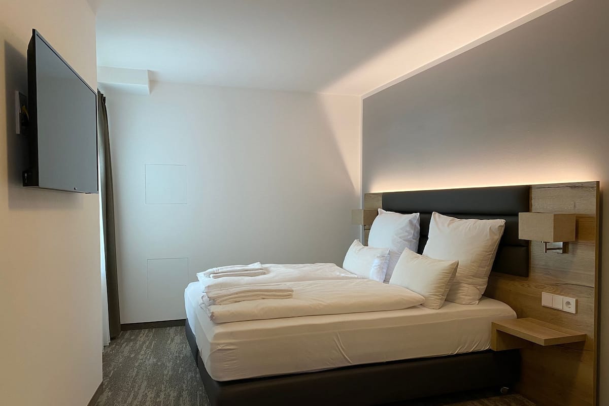 A modern hotel room with a large bed, a flat-screen TV mounted on the wall, and a wooden nightstand.