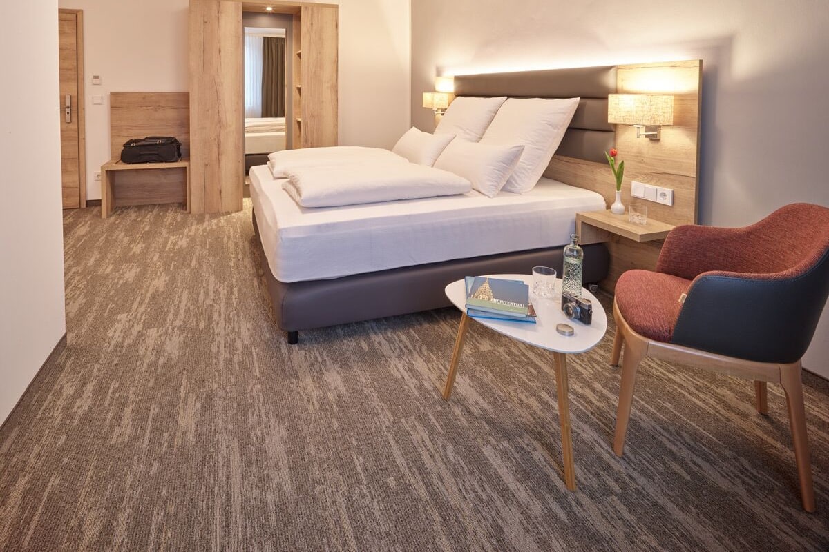 A hotel room with a bed, a chair, a small table, and a nightstand.