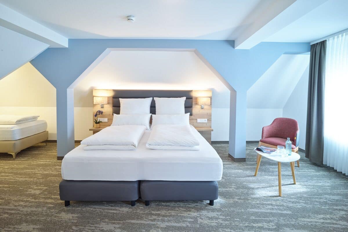 A modern hotel room with a large bed, a red armchair, and a small table.