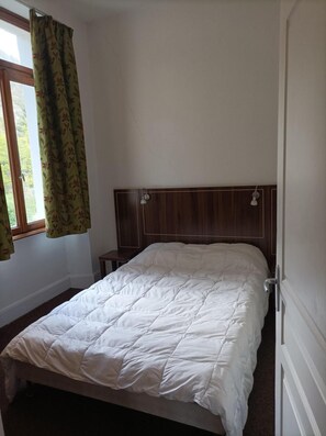 Un dormitorio con cabecera de madera, edredón blanco y ventana con cortinas florales.