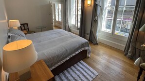 Une chambre à coucher avec un lit, des lampes de chevet, une petite table et une fenêtre avec des rideaux.
