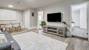 A modern living room with a flat-screen TV, a dining area with a wooden table and chairs, and a large window with a view of the outdoors. - Institute Bliss! Newly Remodeled Family Home! (Colorado Springs)