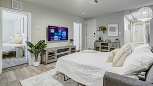 A modern bedroom with a large bed, a TV mounted on the wall, a console table, and a potted plant. - Institute Bliss! Newly Remodeled Family Home! (Colorado Springs)