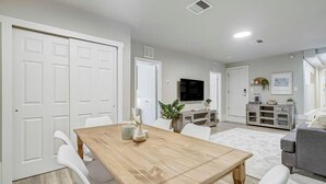 A modern living room with a wooden dining table, white chairs, a grey sofa, and a flat-screen TV mounted on the wall. - Institute Bliss! Newly Remodeled Family Home! (Colorado Springs)