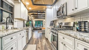 Una cocina moderna con armarios blancos, encimeras de granito y techo de madera.