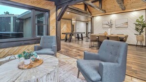 Una habitación amplia con techo alto y vigas a la vista, un comedor con una mesa grande y sillas, y un área de estar con sillones y una mesa de centro.