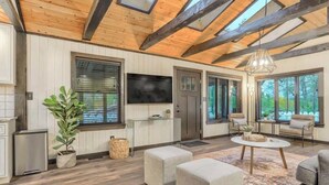 Un salón amplio con vigas de madera, un televisor de pantalla plana grande y asientos cómodos.