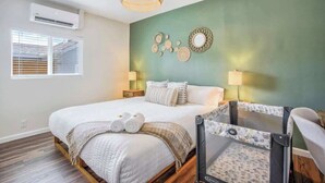 A bedroom with a bed, a crib, a wall-mounted air conditioner, and a window with blinds.