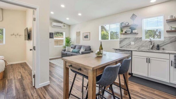 A modern kitchen with a wooden table and bar stools, a built-in oven, and a marble backsplash.