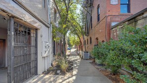A narrow alleyway with buildings on either side, a fire escape, and a small tree.